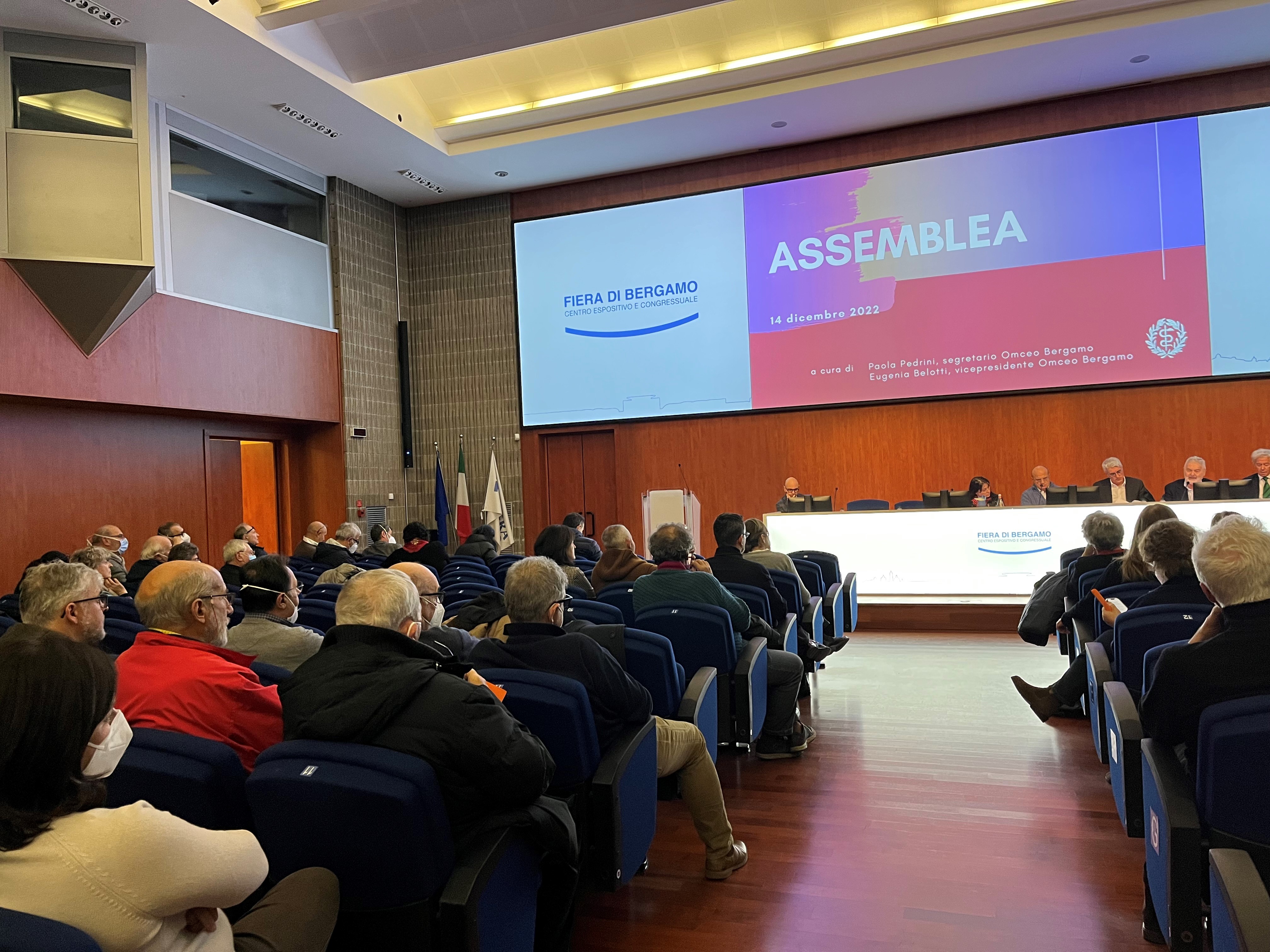 immagine raffigurante uno scatto dell'assemblea dello scorso anno con scorcio della sala e dei partecipanti e tavolo dei relatori